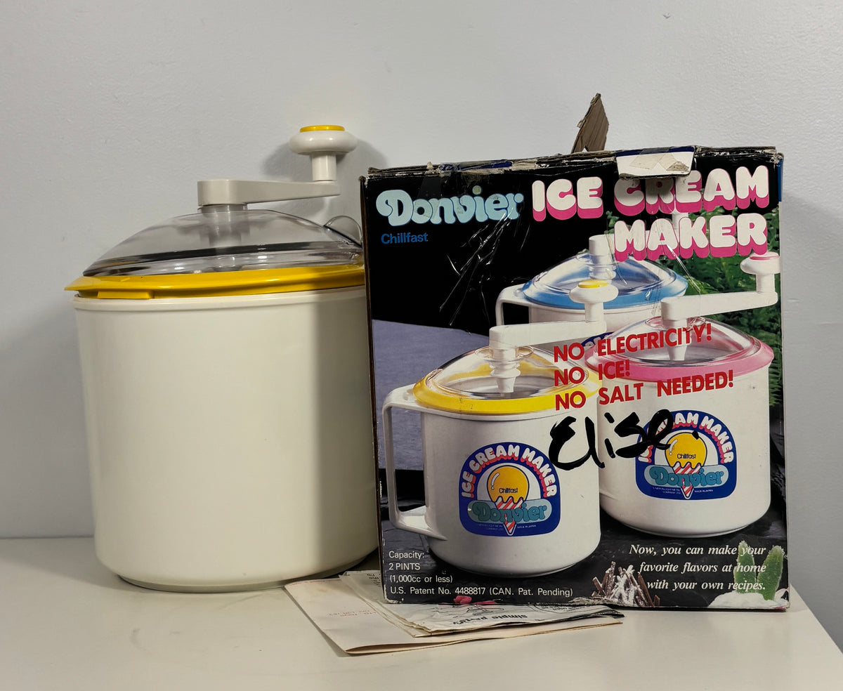 A vintage Donvier ice cream maker set displayed on a tabletop against a plain wall, including the creamer container, the retail box, and handwritten price marking on the package.