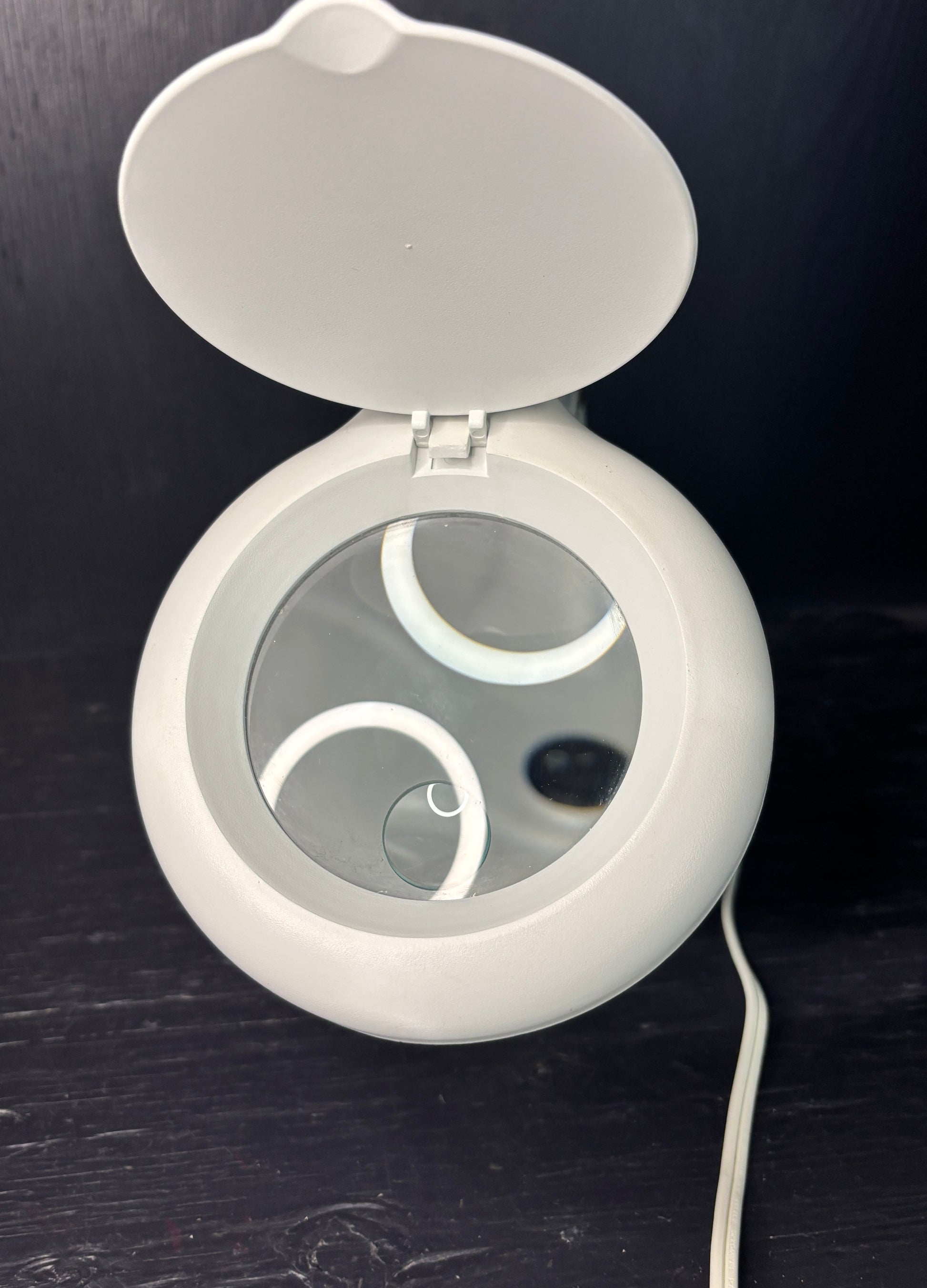 Round white device with a mirror on a dark surface