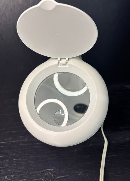 Round white device with a mirror on a dark surface