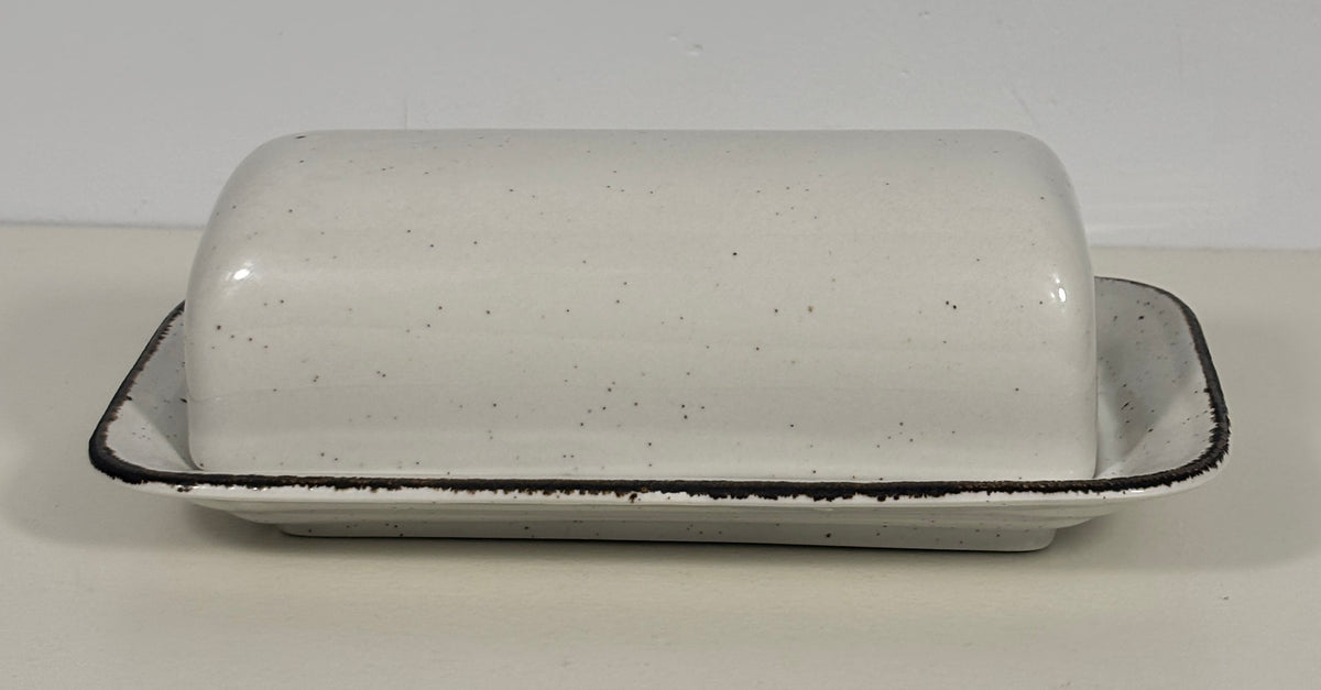 A speckled white ceramic butter dish with a matching lid, featuring a black rim, set against a plain light background.