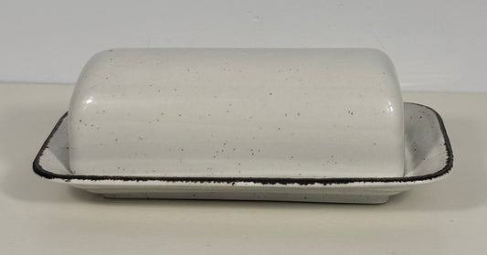 A speckled white ceramic butter dish with a matching lid, featuring a black rim, set against a plain light background.