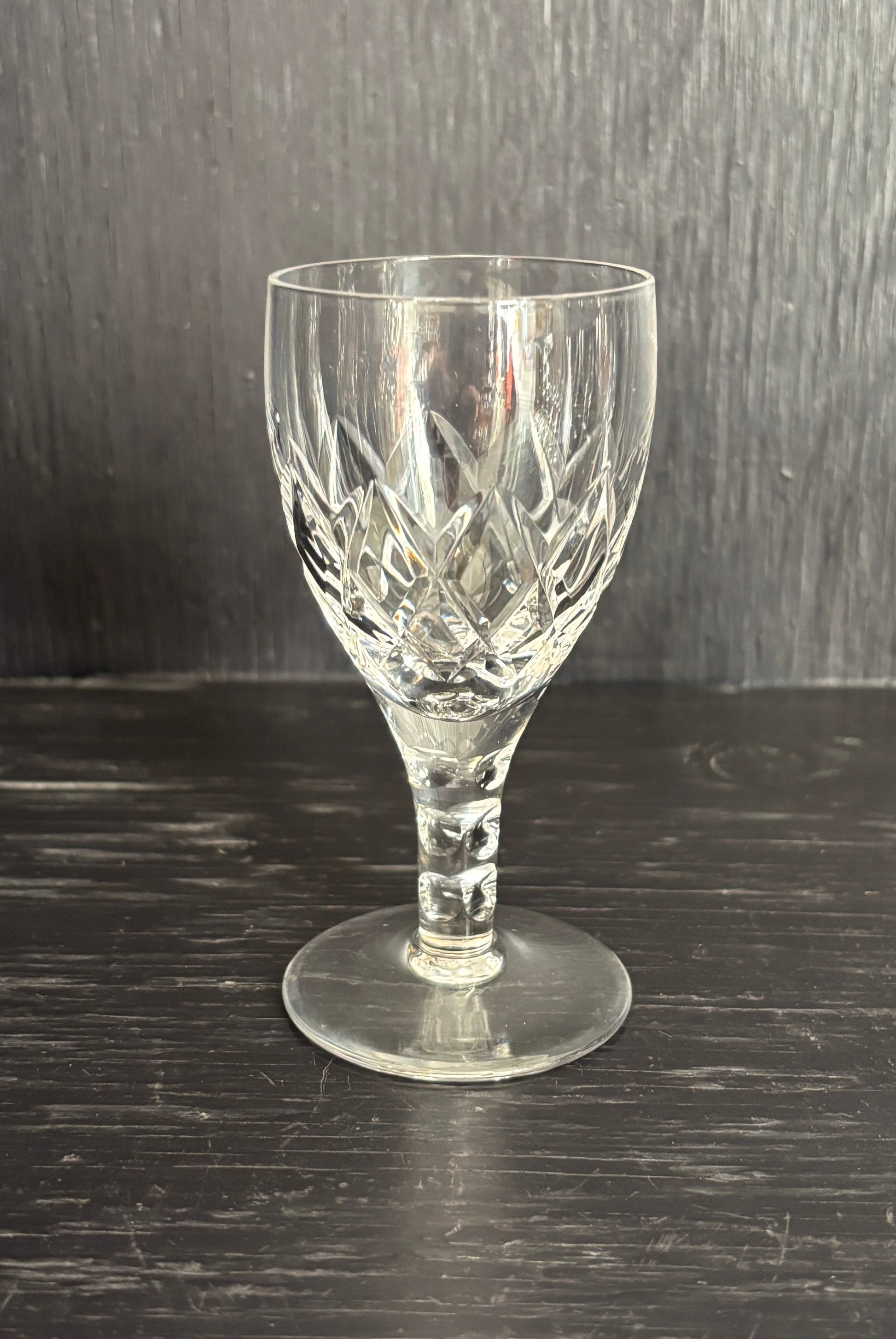 Clear glass wine glass with cut patterns on a dark wooden surface
