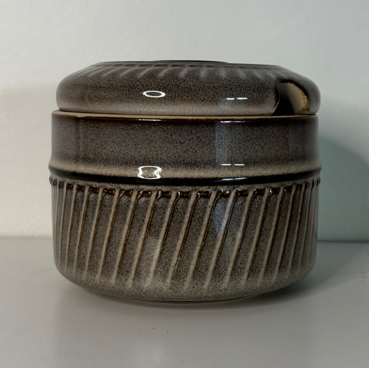 Stoneware jar with ribbed texture and lid on a plain background
