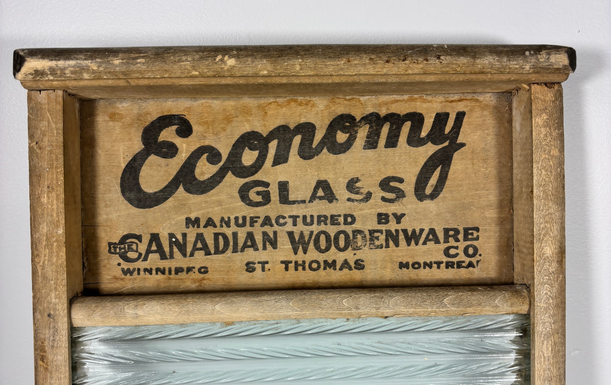Vintage wooden washboard with a glass window and printed text reading 'Economy Glass' and 'Manufactured by the Canadian Woodenware Co.' on a light background.