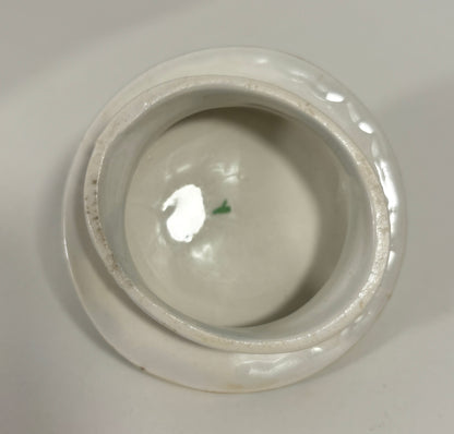 A top-down view of a white ceramic lidded container or small bowl, showing a glossy interior and a slightly worn, rustic rim against a neutral light gray background.