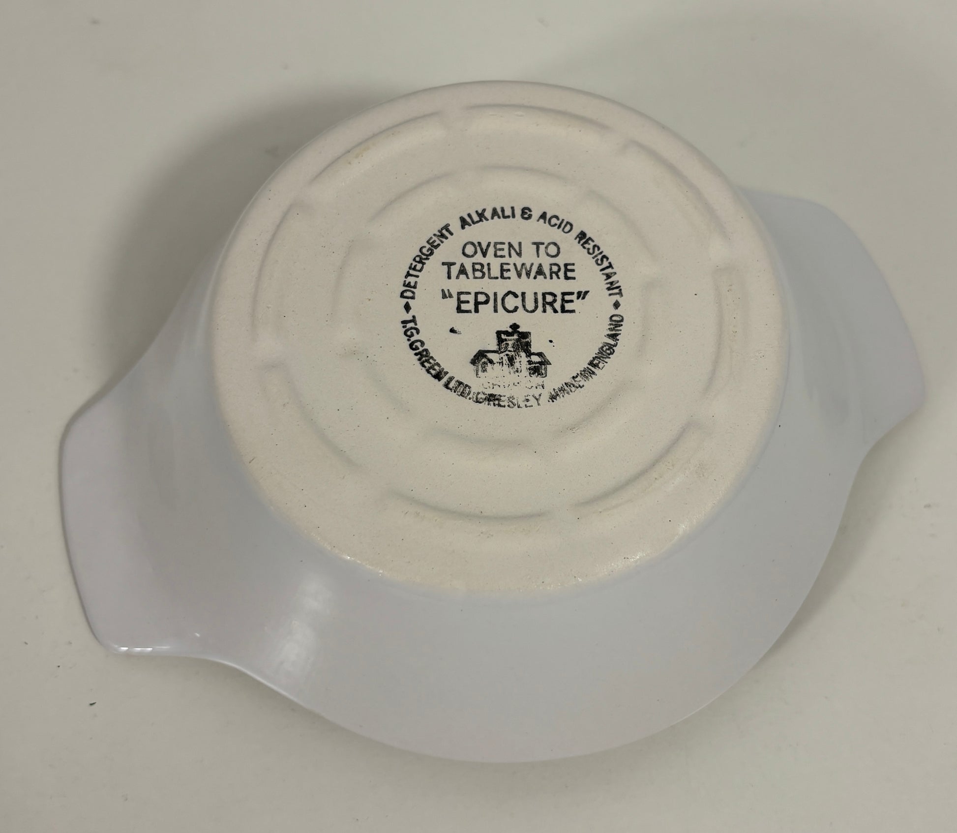 The bottom of a white ceramic dish or bowl with a printed black label reading 'EPICURE' and 'OVEN TO TABLEWARE', photographed on a plain light background.