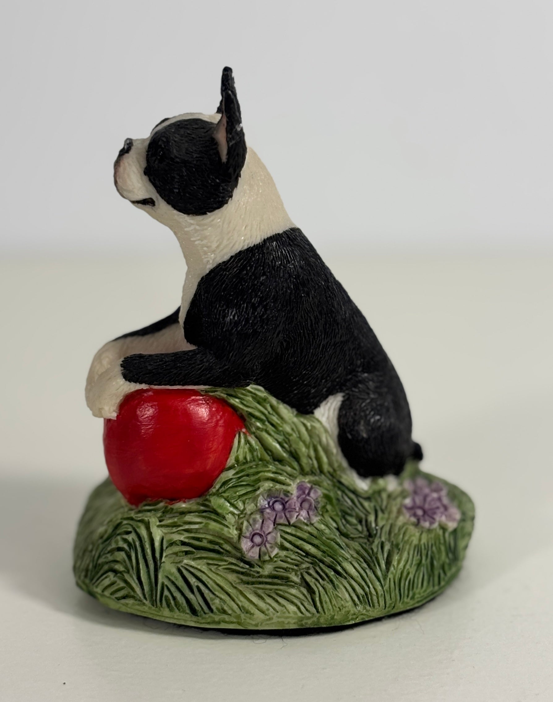 Dog figurine sitting on a red ball with grass and flowers on a white background