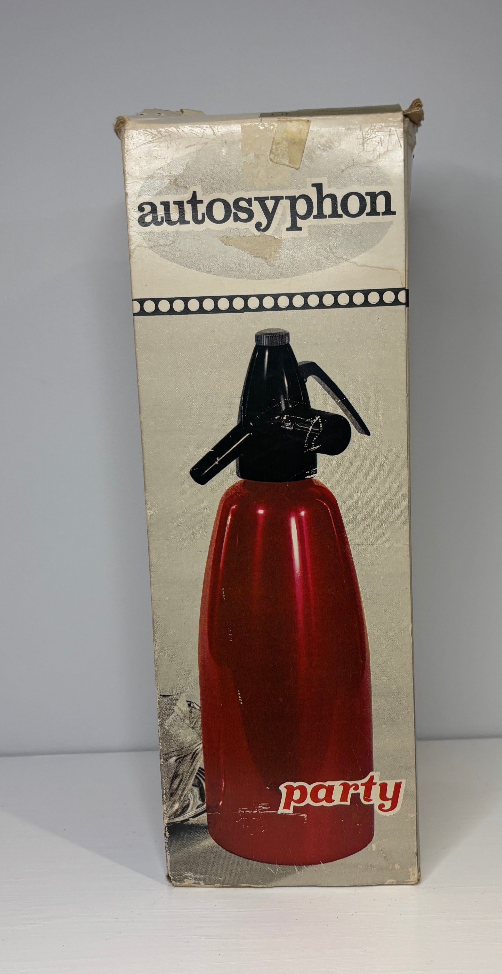 Vintage autosyphon party bottle packaging with red bottle and black nozzle on a gray background