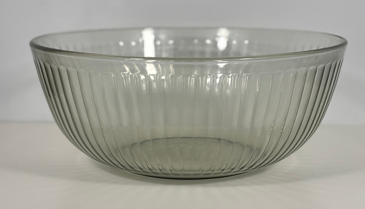 A clear ribbed glass bowl with a flared rim, photographed against a plain light gray background.