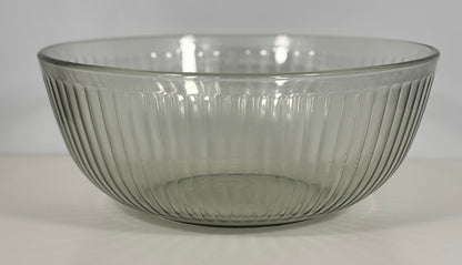 A clear ribbed glass bowl with a flared rim, photographed against a plain light gray background.