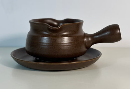 Brown gravy boat with handle on a matching saucer against a light background