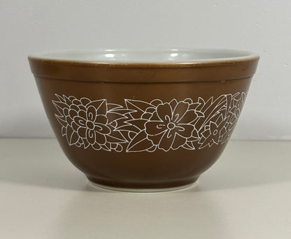 A brown mixing bowl with a white floral line pattern around the outside and a white interior, shown against a neutral light gray background.