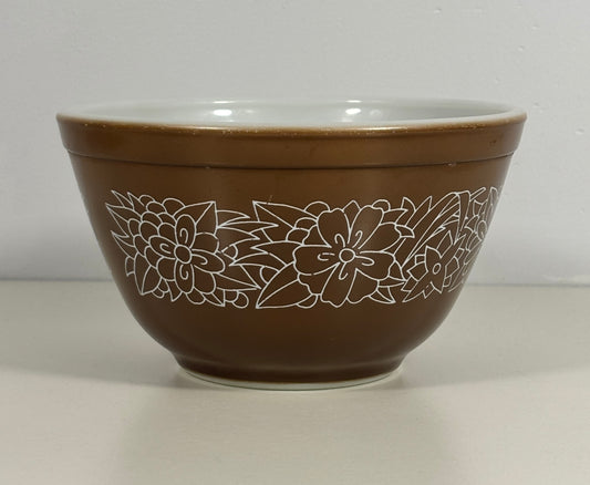 A brown mixing bowl with a white floral line pattern around the outside and a white interior, shown against a neutral light gray background.