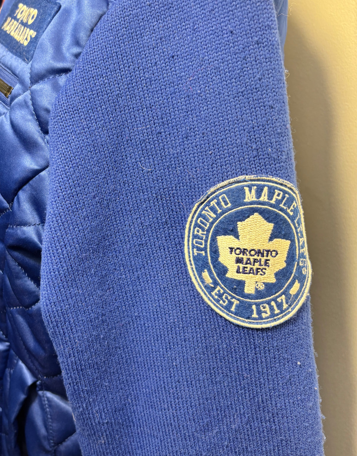 Close-up of a blue knit sleeve featuring an embroidered circular Toronto Maple Leafs patch in yellow and blue.
