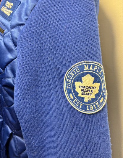 Close-up of a blue knit sleeve featuring an embroidered circular Toronto Maple Leafs patch in yellow and blue.