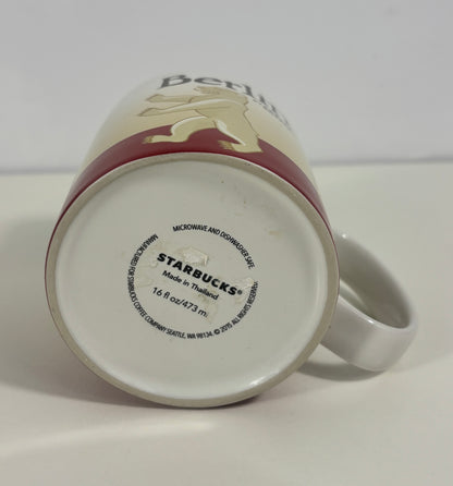 A white ceramic Starbucks mug shown upside down, displaying the printed bottom base with 'STARBUCKS Made in Thailand' and a gold rooster logo. The mug features a dark red band and partial gold graphic text on a white background.