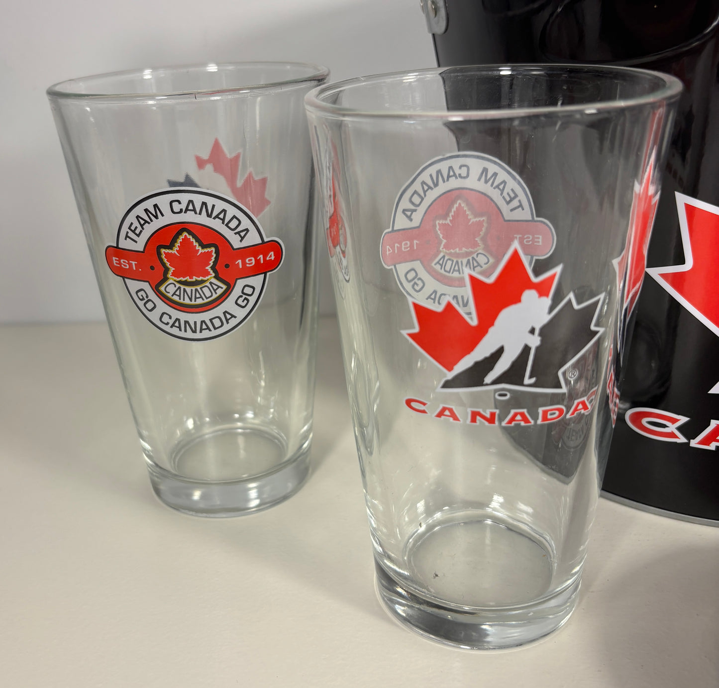 Two clear glasses with Team Canada logos on a white surface.