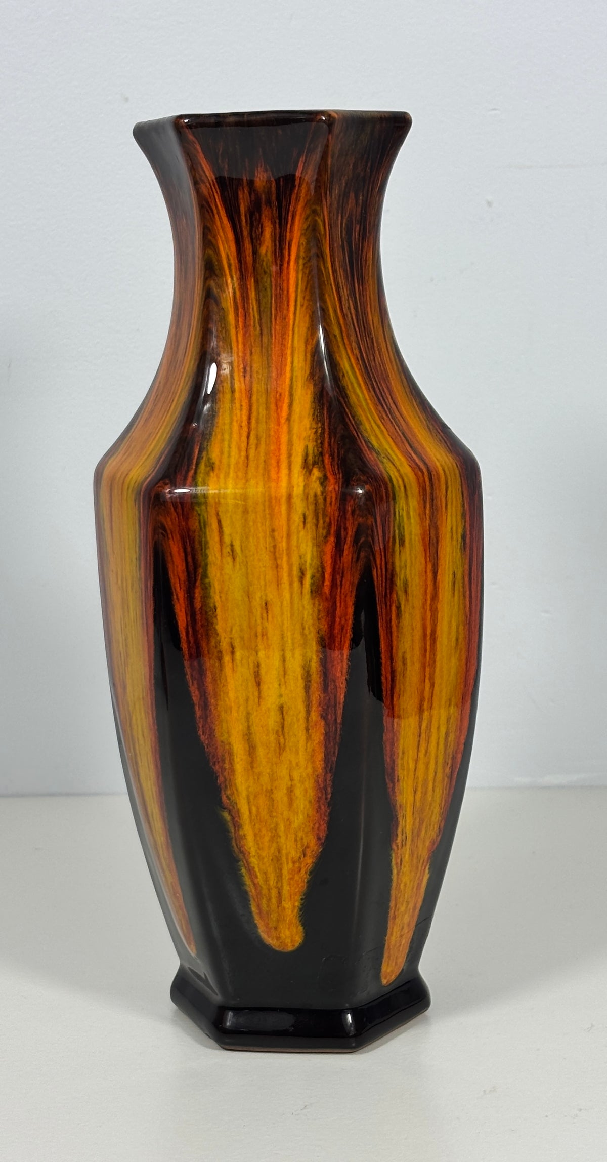 A glossy ceramic vase with a flared neck and hexagonal base, featuring a marbled glaze pattern of black, orange, and yellow.