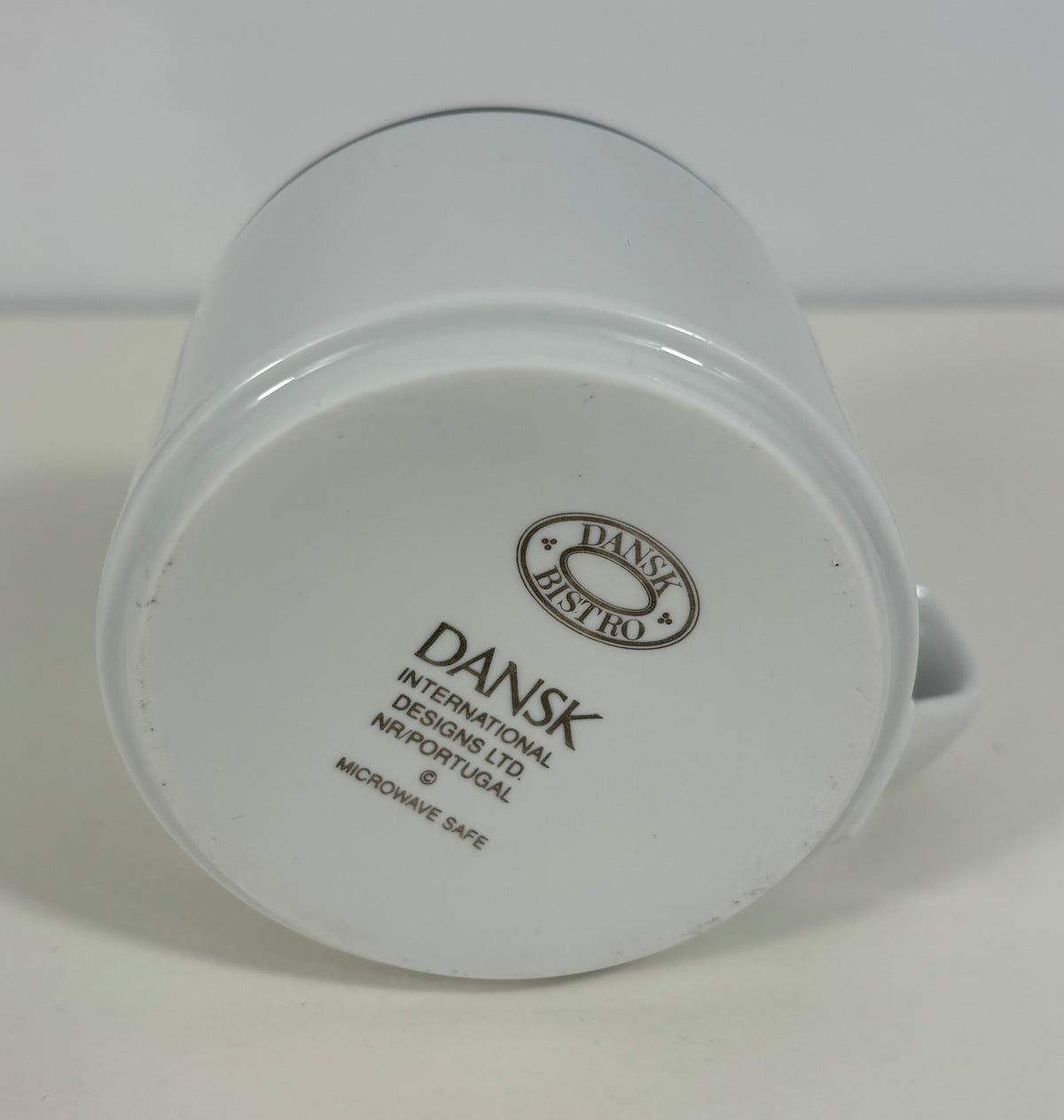 White ceramic mug shown upside down, displaying the printed bottom label with the Dansk Bistro brand logo and text.