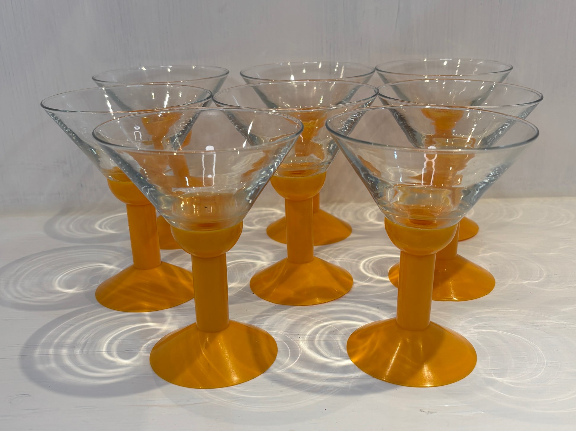 Set of six clear glass cocktail glasses with yellow stems on a white surface.
