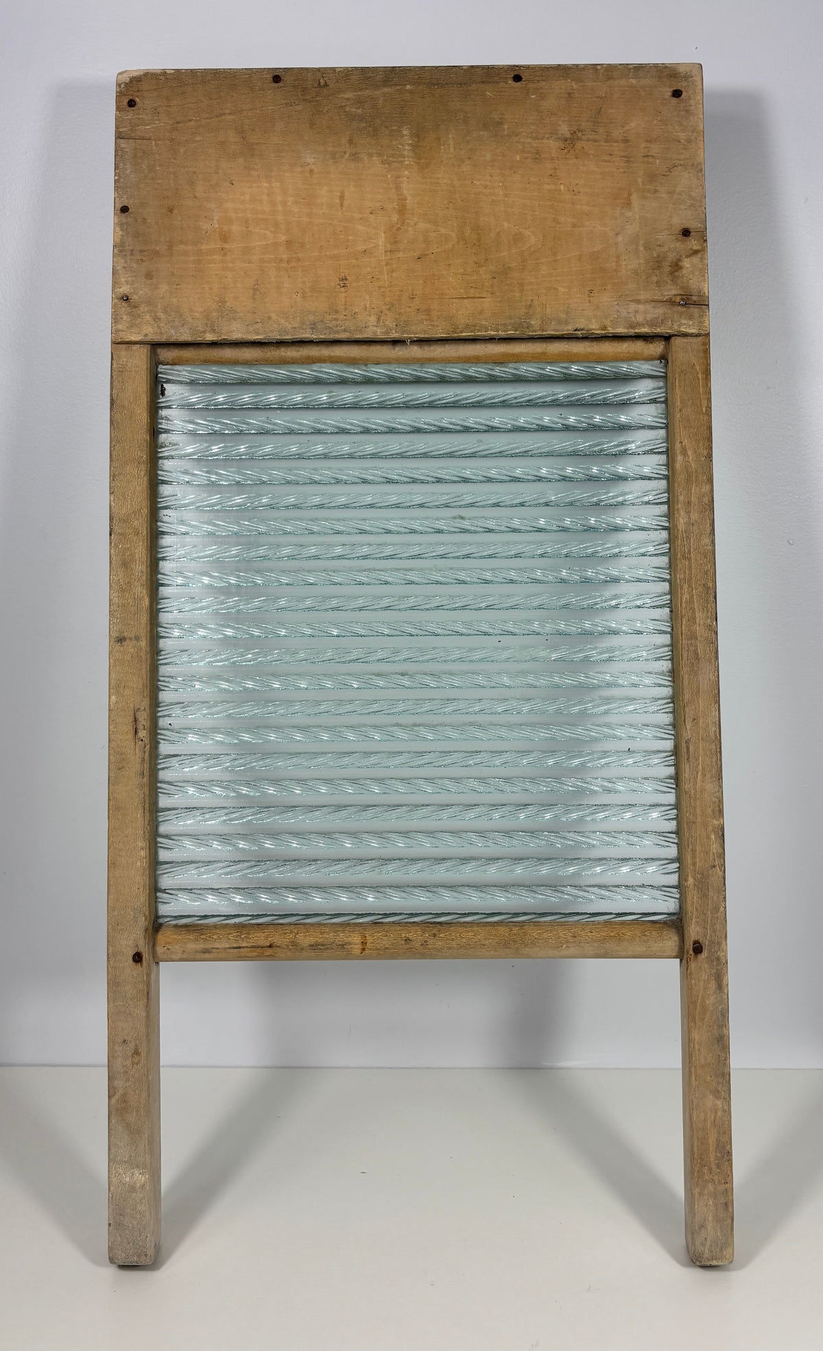 A vintage wooden washboard with a ribbed glass or metal plate and a rustic light brown wood frame, photographed against a plain light gray background.