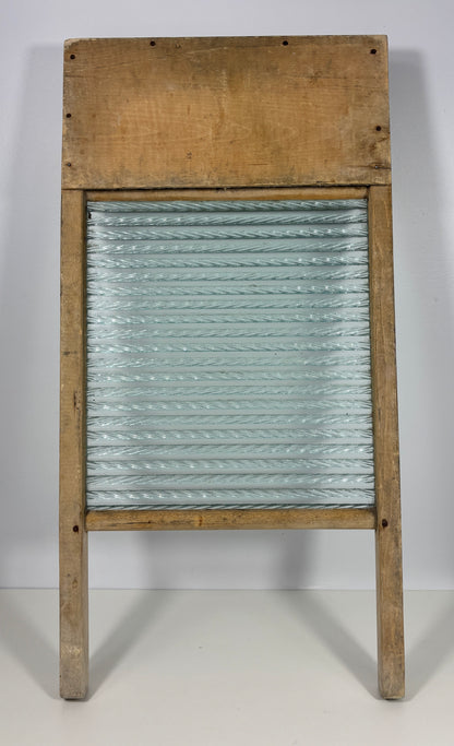 A vintage wooden washboard with a ribbed glass or metal plate and a rustic light brown wood frame, photographed against a plain light gray background.