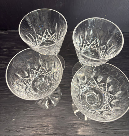 Four crystal glasses with engraved designs on a dark wooden surface