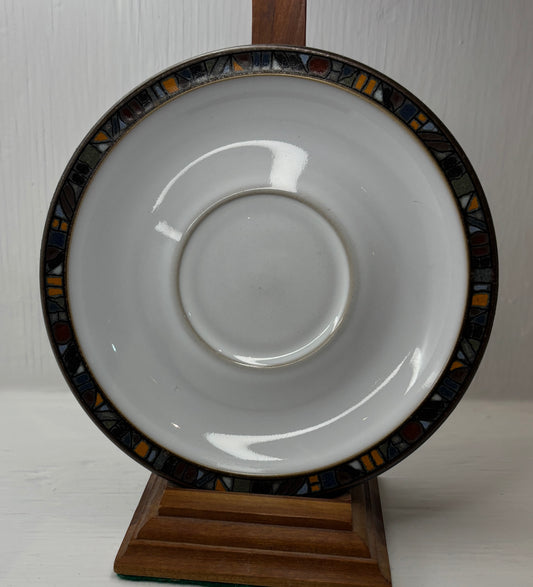 White saucer with decorative black rim on a wooden stand against a white background