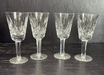 Four crystal sherry glasses on a dark surface with a dark background
