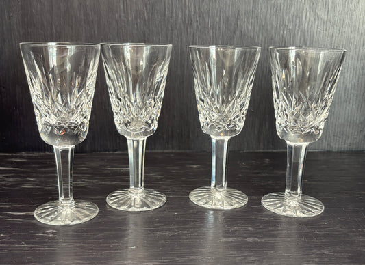 Four crystal sherry glasses on a dark surface with a dark background