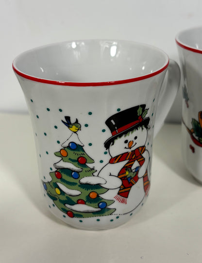 A white ceramic mug with a red rim, decorated with a festive winter scene featuring a snowman in a black top hat and red striped scarf next to a decorated Christmas tree with colorful ornaments.
