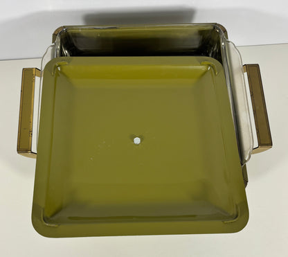 An olive green square glass baking dish with clear glass sides and gold-toned metal handles, photographed from a top-down angle on a white surface.