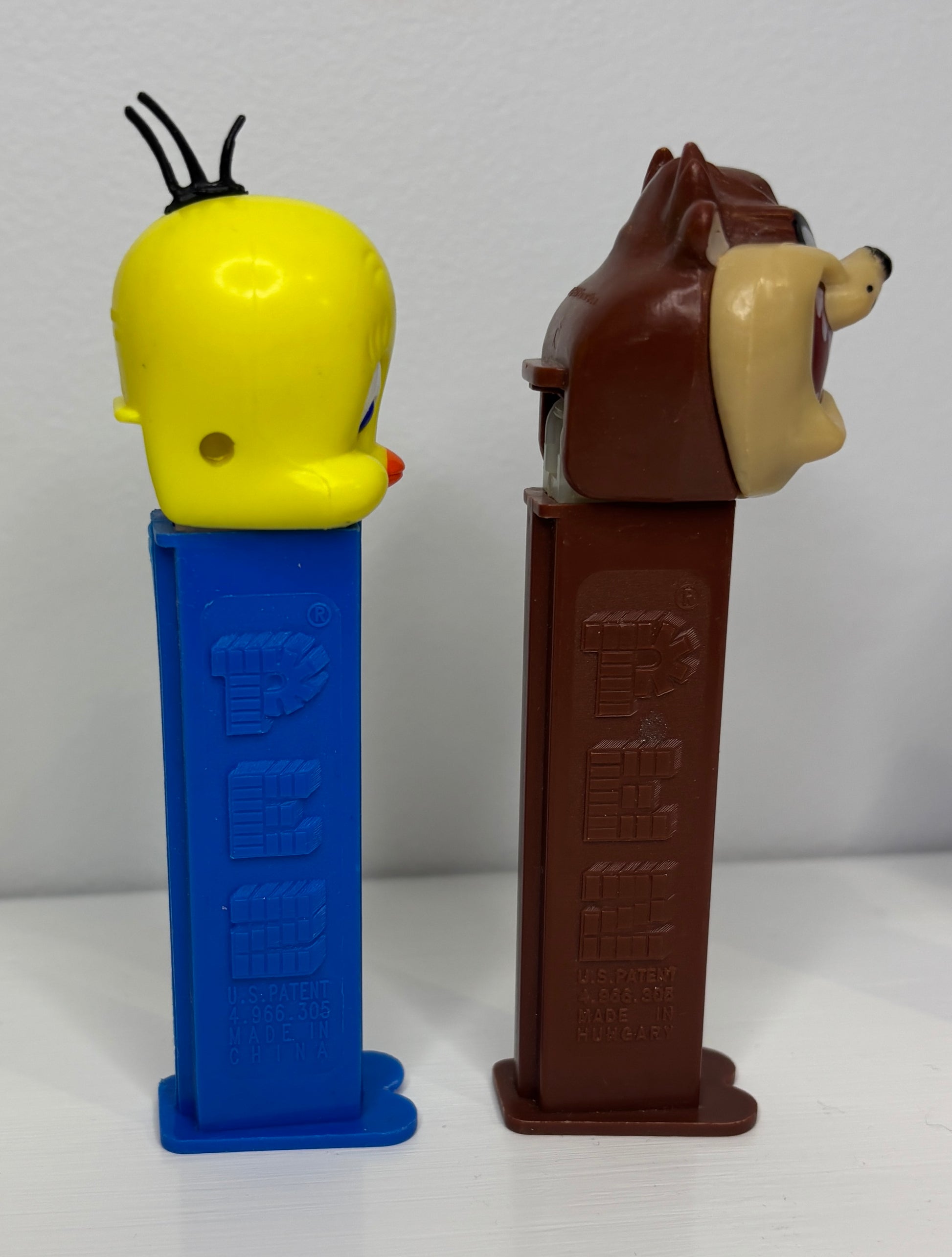 Two PEZ dispensers, one yellow and blue, the other brown and red, on a white background.