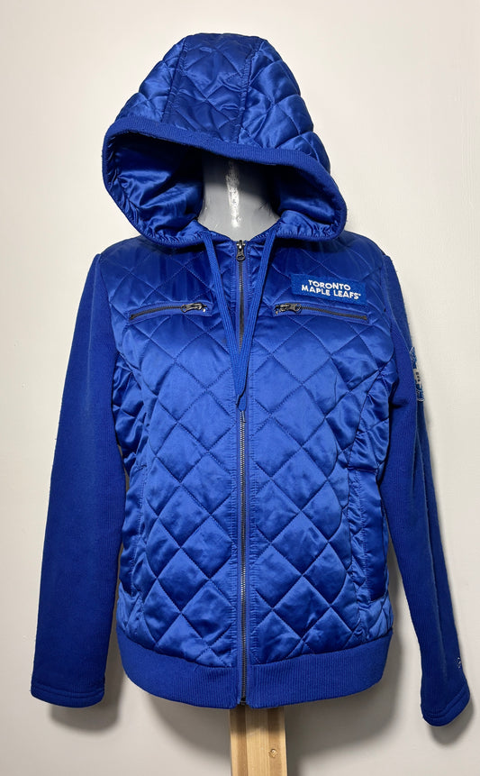 A royal blue quilted zip-up hooded jacket displayed on a mannequin torso against a plain off-white wall. The jacket features diamond-quilted panels, zippered chest pockets, and a white embroidered logo reading 'TORONTO MARISE LEAFS' on the left chest.