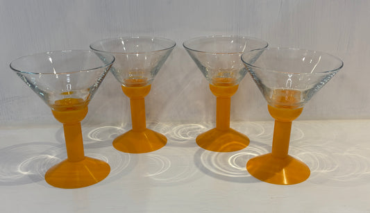 Four cocktail glasses with orange stems on a white surface