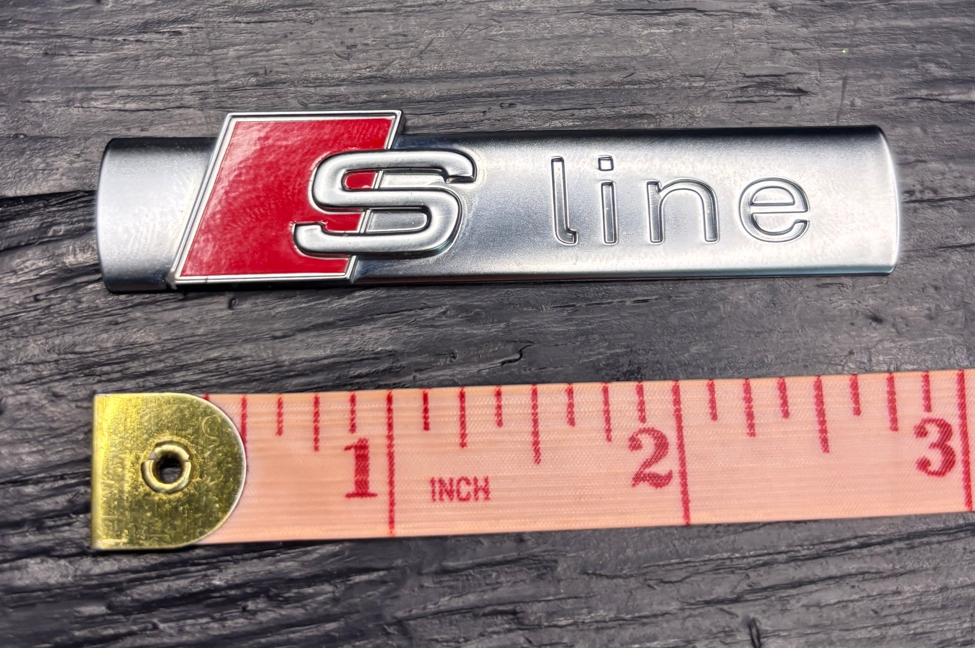 Audi S line badge with a ruler for scale on a wooden surface
