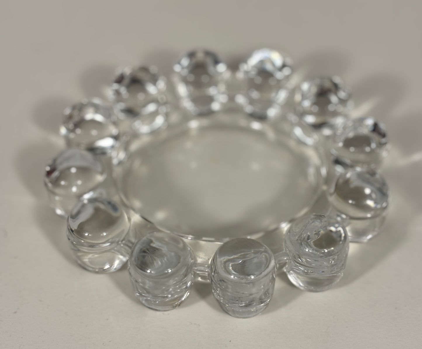 A clear glass ring with multiple small cylindrical beads around the outer edge, photographed on a plain light background.