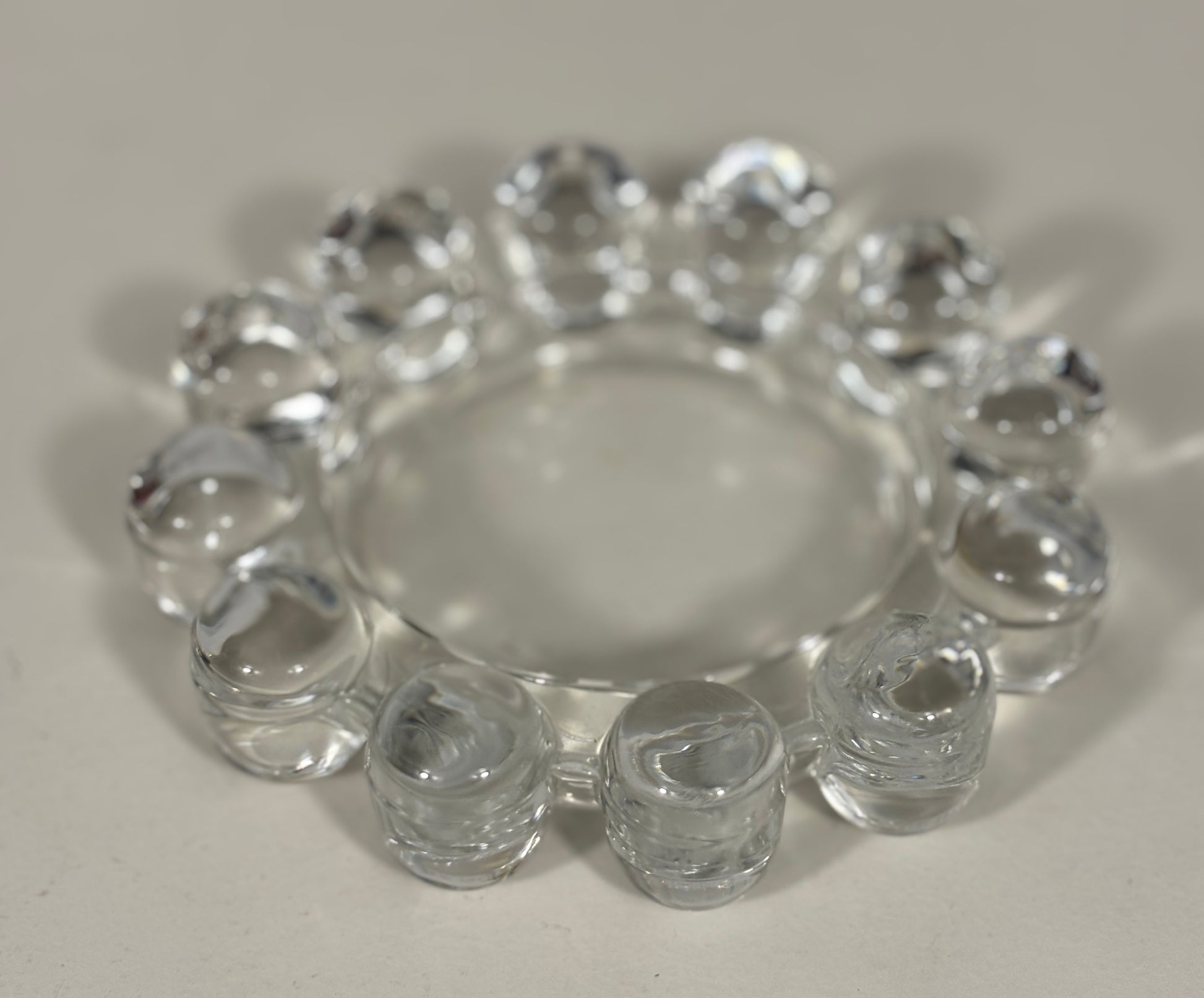 A clear glass ring with multiple small cylindrical beads around the outer edge, photographed on a plain light background.