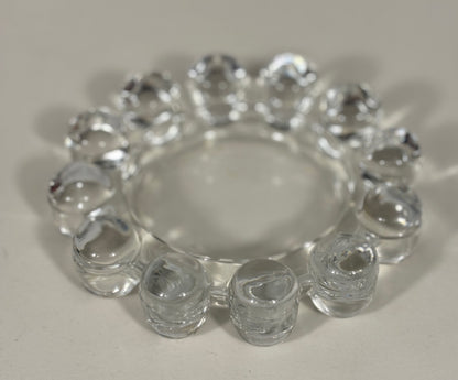 A clear glass ring with multiple small cylindrical beads around the outer edge, photographed on a plain light background.
