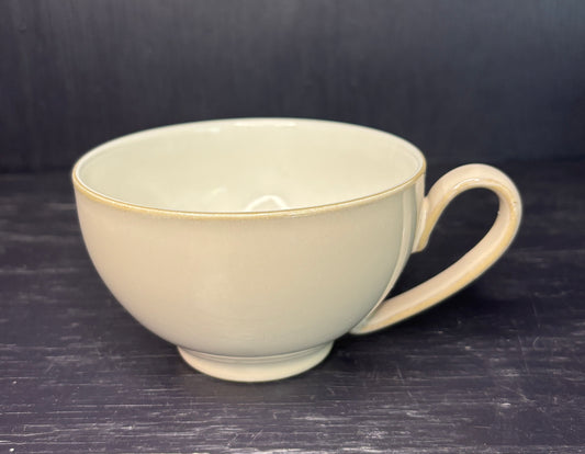 Beige ceramic teacup with a handle on a dark surface
