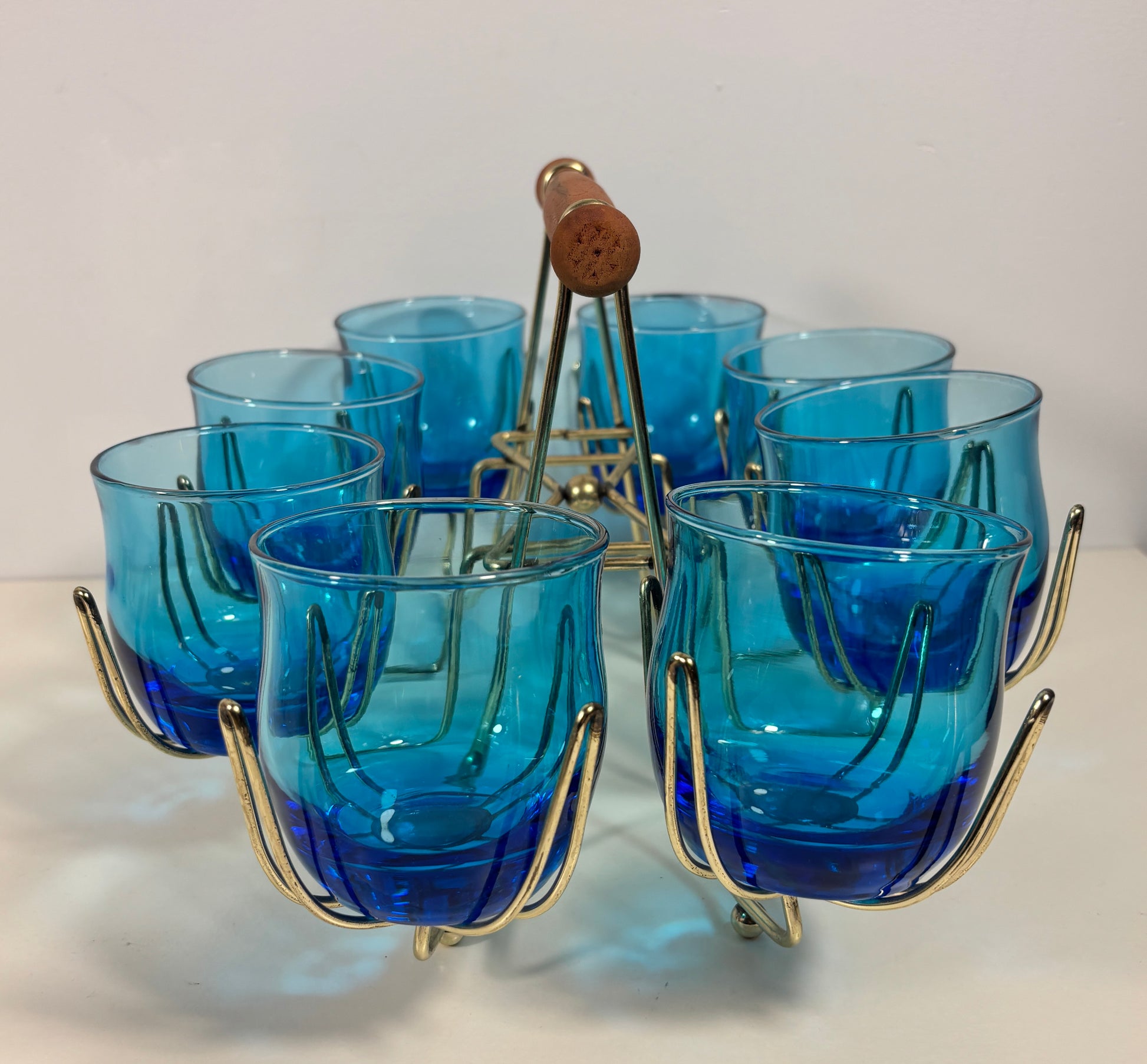 A set of six cobalt blue ribbed glass shot glasses with gold-finished metal wire holders, arranged in a circular pattern on a white surface with a white background.