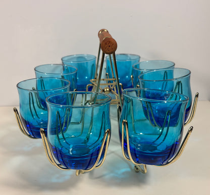 A set of six cobalt blue ribbed glass shot glasses with gold-finished metal wire holders, arranged in a circular pattern on a white surface with a white background.