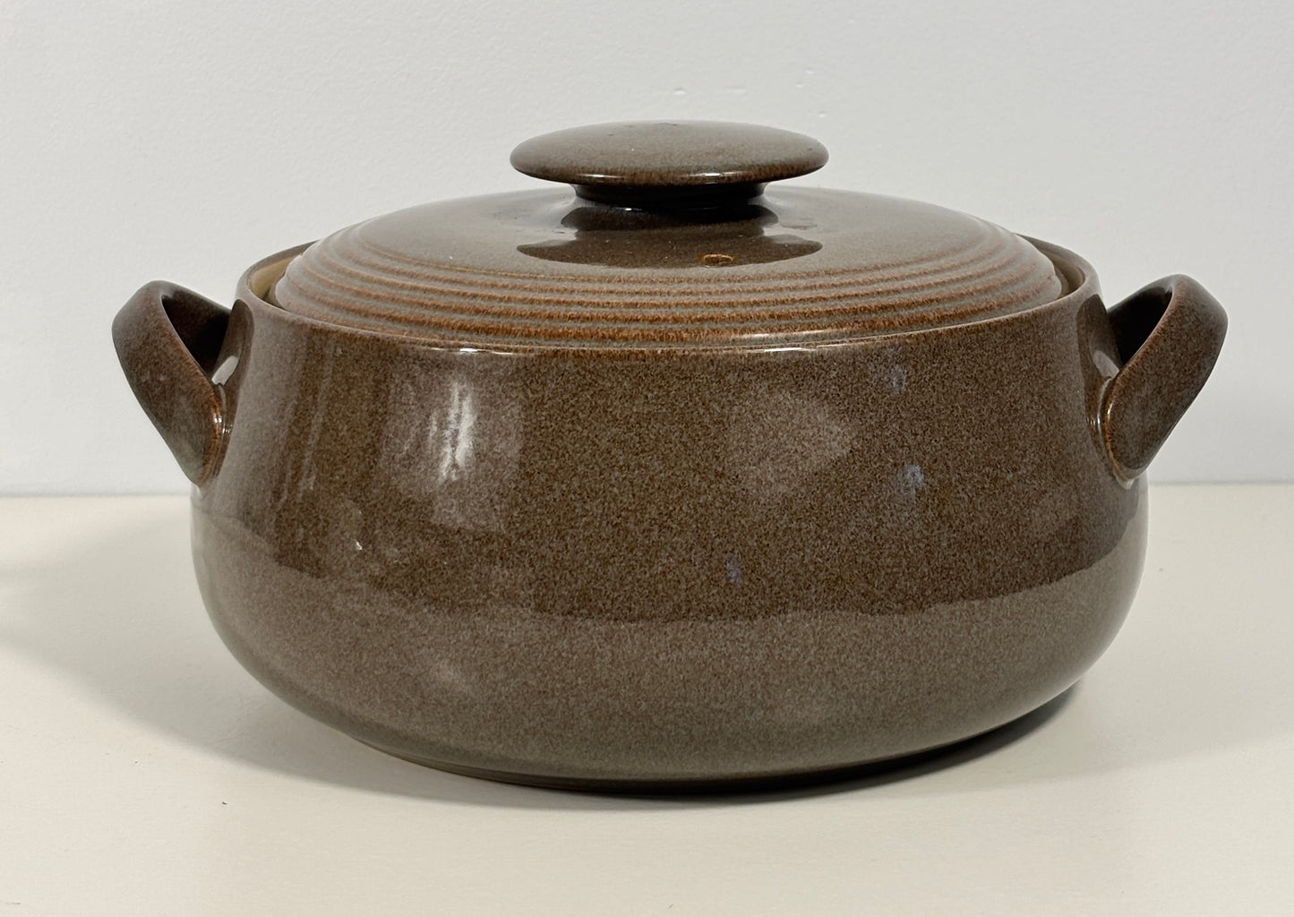 A brown ceramic lidded casserole pot with two side handles, shown on a plain white background.