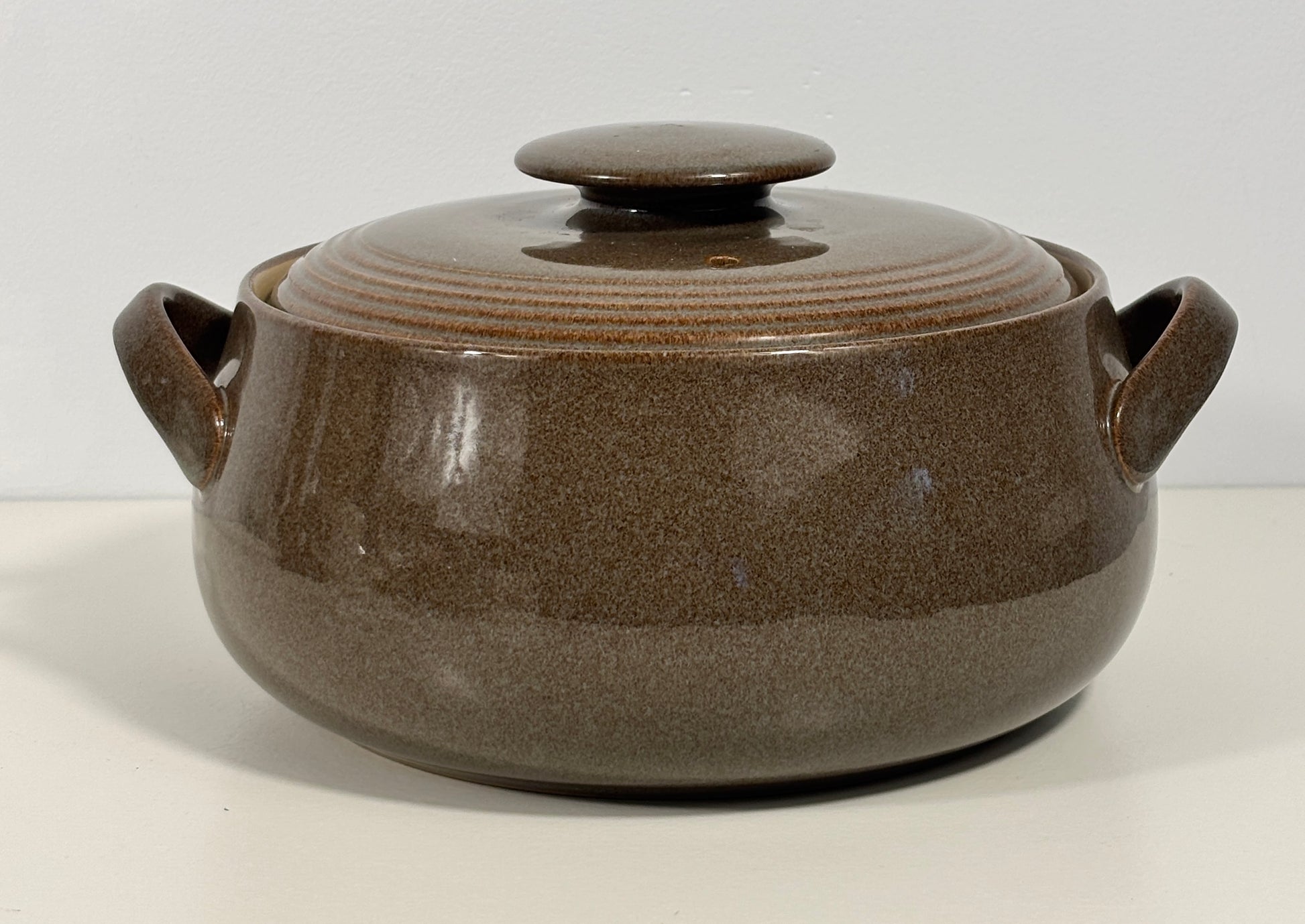 A brown ceramic lidded casserole pot with two side handles, shown on a plain white background.