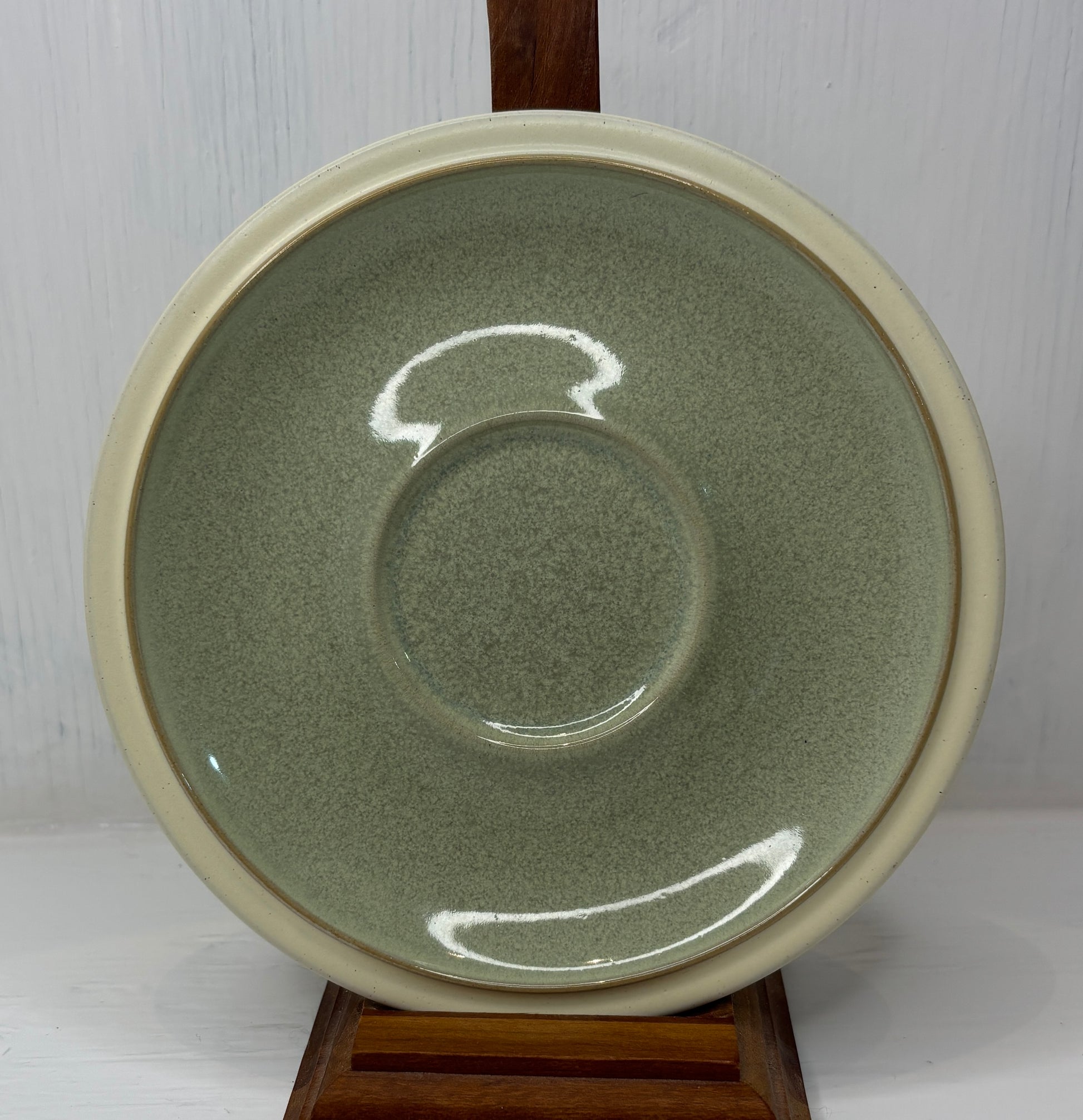 Green ceramic plate with beige rim on a wooden stand against a white background