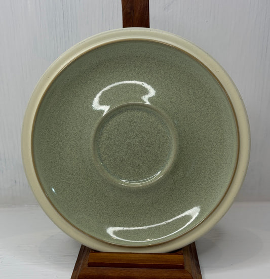 Green ceramic plate with beige rim on a wooden stand against a white background