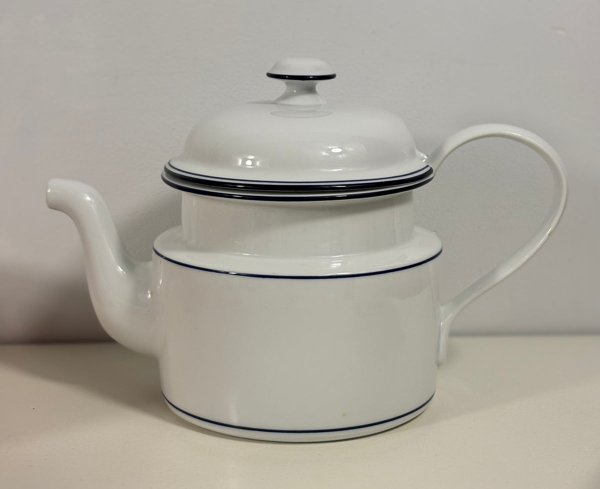 A white ceramic teapot with a lid, featuring thin dark blue stripes as accents, set against a plain light gray background.