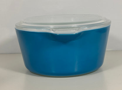A bright blue glass casserole dish with a clear glass lid, photographed against a neutral light gray background.