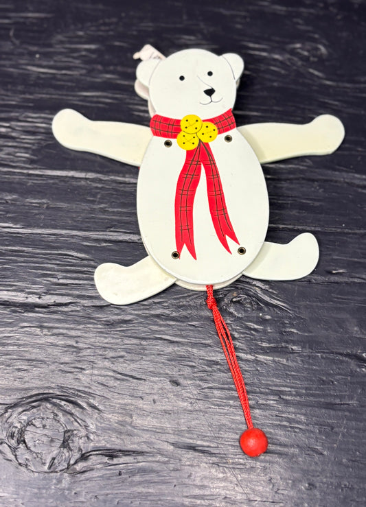 White bear-shaped wooden toy with a red ribbon and yellow buttons on a dark wooden surface