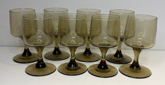 Set of nine smoked glass wine glasses on a white background